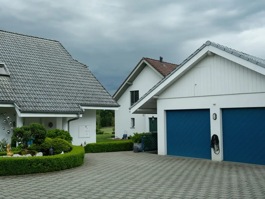 Maison blanche à double garage, allée pavée et haies taillées