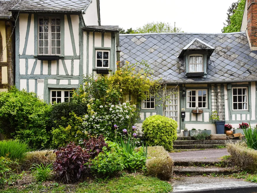 Maison normande à colombages et toit d’ardoise, devant un jardin fleuri